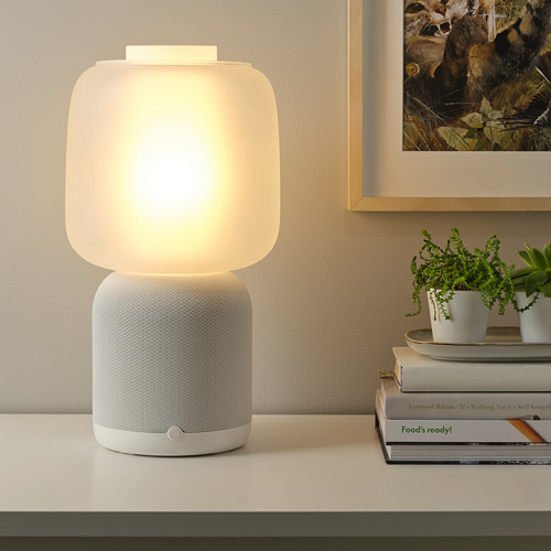 Moderna lámpara wifi y altavoz con luz cálida, plantas, libros e imágenes.