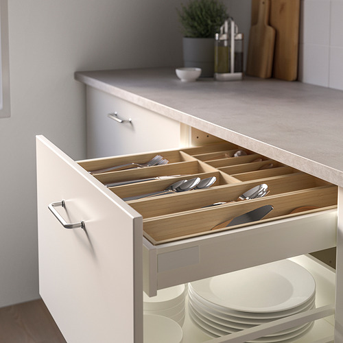 Cajón de cocina abierto con bandeja de madera para cubiertos, organizando cuidadosamente los utensilios. Cajón ancho, platos apilados debajo.