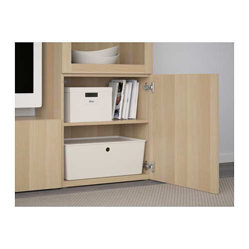 Armario de madera clara con puerta abierta, que exhibe cajas de almacenamiento y revistas en estantes, cajón cerrado debajo.