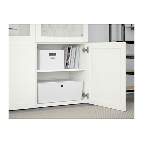 Mueble blanco con estantes ajustables; Un estante tiene una caja de almacenamiento blanca y revistas. La puerta tiene bisagras de cierre suave.