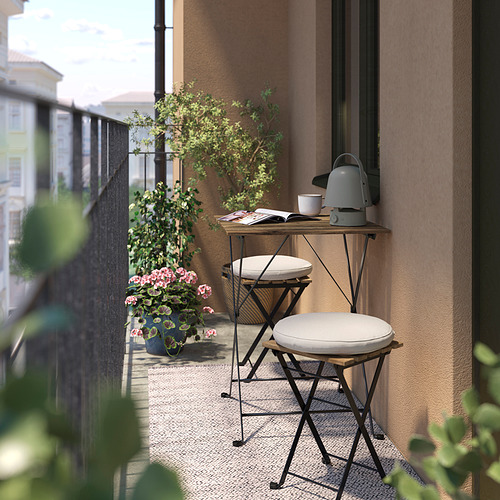Pequeño balcón con dos taburetes TÄRNÖ blancos y una mesita metálica, con una tetera gris y flores rosas en macetas.