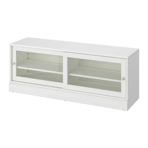 Un banco de tv HAVSTA blanco con puertas correderas de vidrio, hecho de pino macizo, que ofrece un diseño rústico y moderno para el almacenamiento en el hogar.