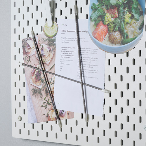 Tablero perforado blanco con clips de hidrógeno que sostienen recetas y utensilios.