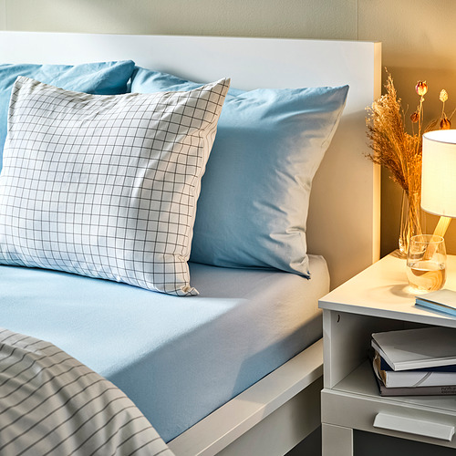 Sábana ajustable azul en la cama con almohada de cuadros. 100% algodón, colchón grueso, libros de noche y lámpara. Ambiente acogedor y acogedor para dormir.