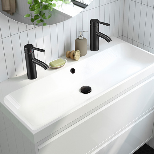 Lavabo de baño moderno con elegante grifo negro y palanca para la eficiencia del agua, flanqueado por dispensador de jabón y accesorios sobre encimera blanca.