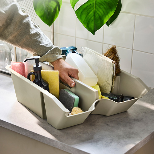 Persona sosteniendo un contenedor de almacenamiento SORTERA lleno de esponjas, dispensador de jabón y cepillos sobre una encimera.