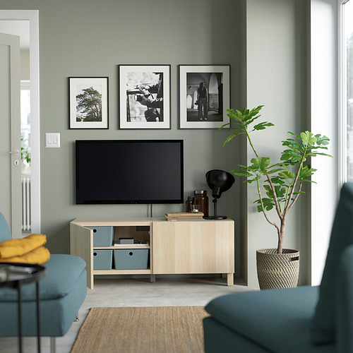Sala de estar moderna con paredes verdes y banco de televisión BESTÅ, estantes ajustables, tres fotos, planta alta en cesta.
