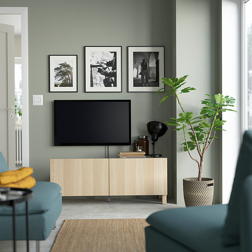 Sala de estar moderna con banco de televisión de madera clara BESTÅ, paredes verde salvia, arte, plantas, sofá verde azulado y almacenamiento.