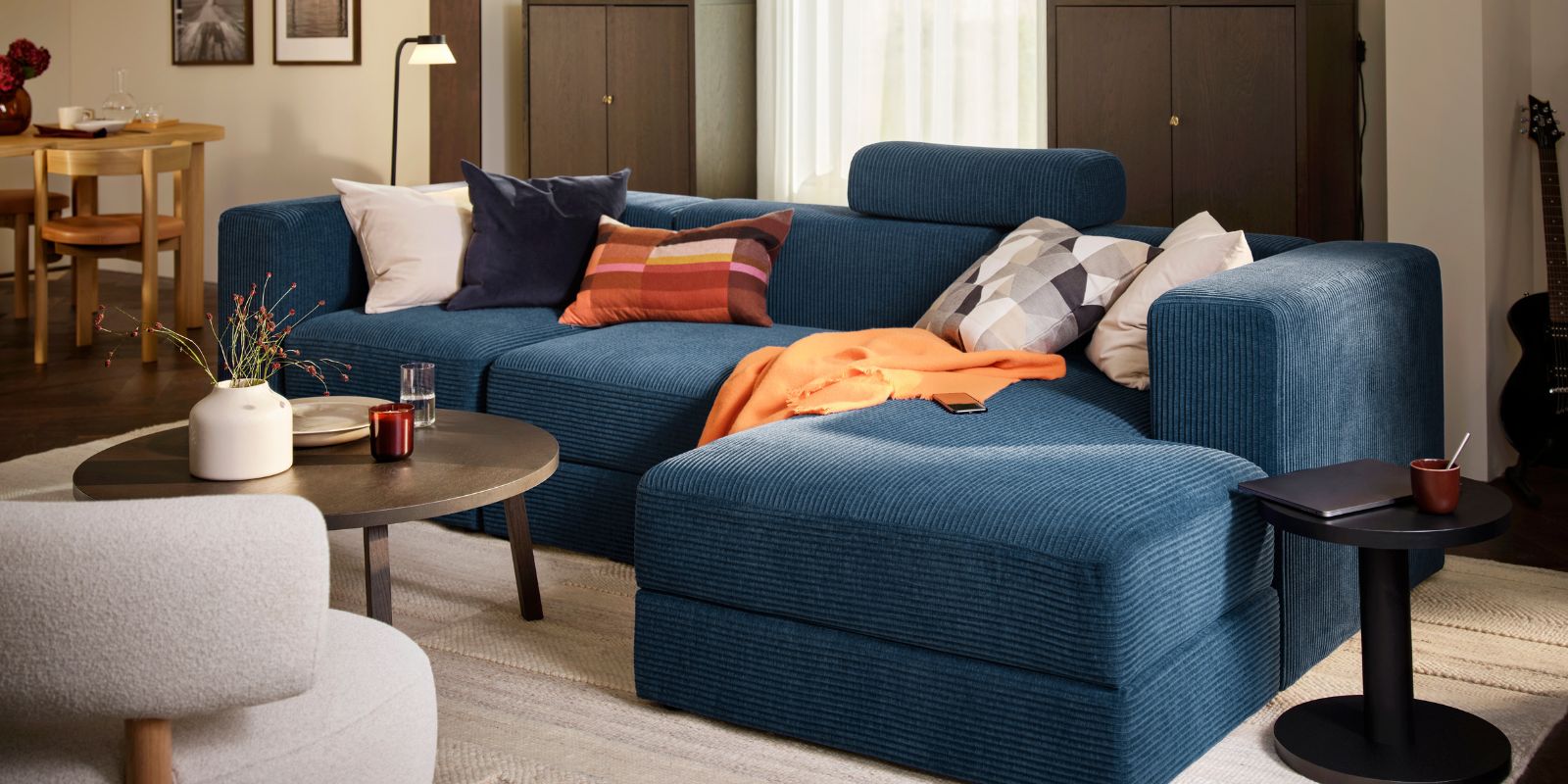 A living room with a dark-blue JÄTTEBO four-seat sofa with chaise longue, complemented by a round table and decorative items.