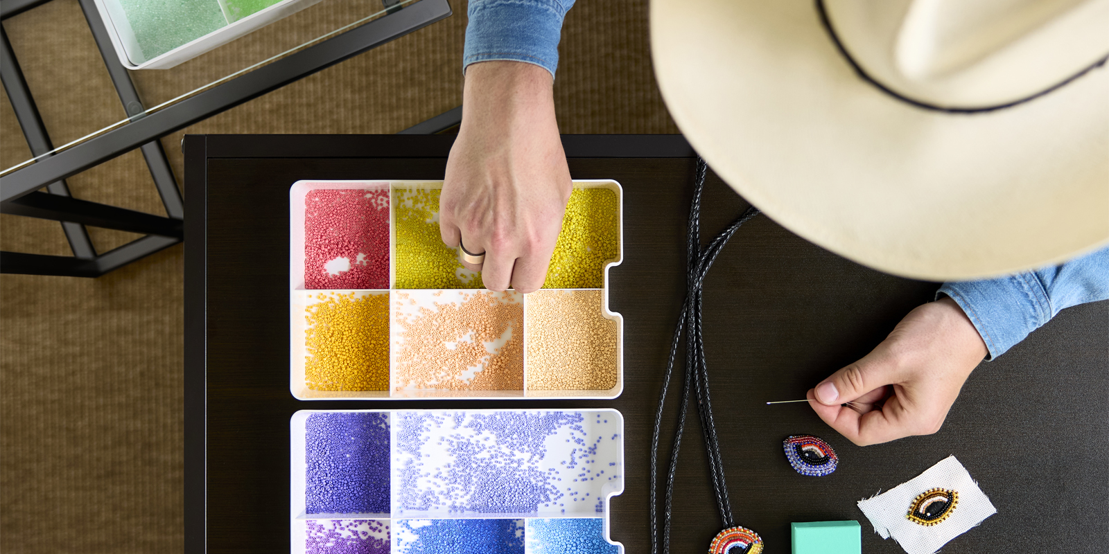 Top view of person crafting with colorful pearls stored in a white KUGGIS insert with five compartments on a table.