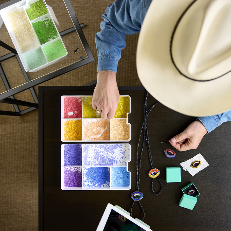 Top view of person crafting with colorful pearls stored in a white KUGGIS insert with five compartments on a table.