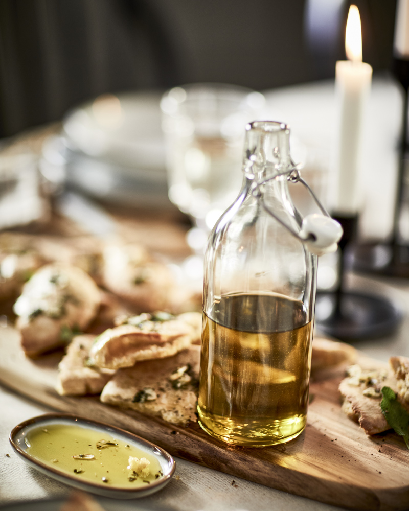 Glass bottle with olive oil on a wooden board with bread, candles, and minimalist tableware – cozy dining setup.