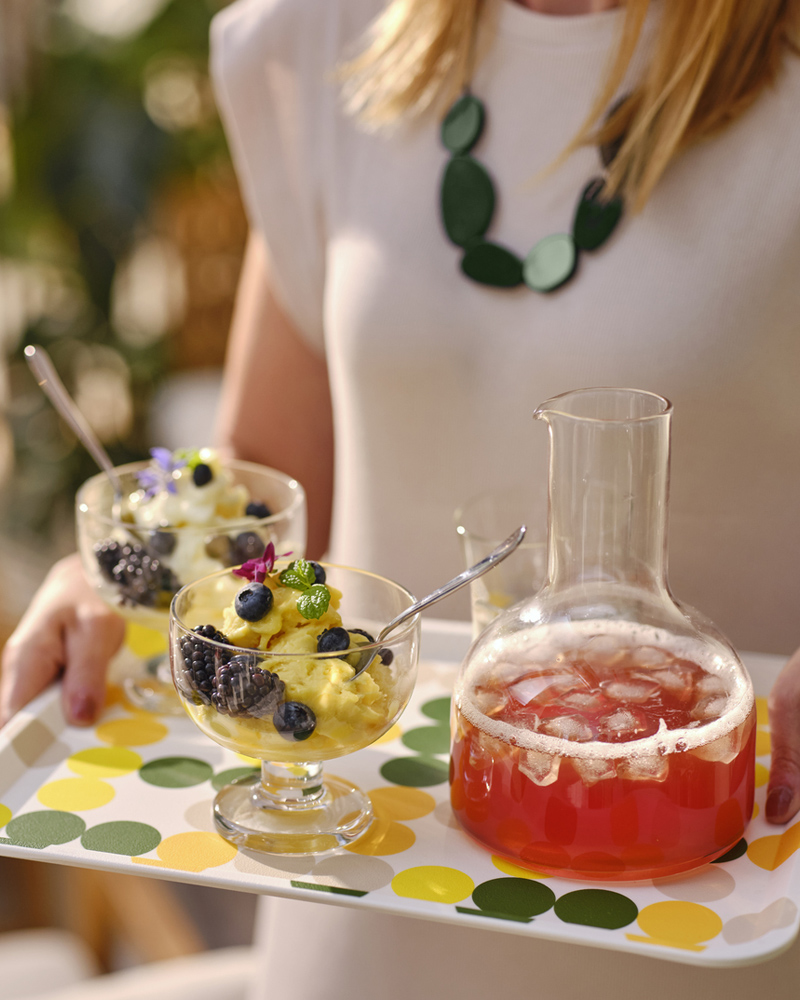 Person serving berry-topped ice cream and iced drink on a colorful tray.
