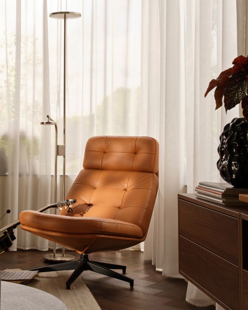 A living-room corner with a golden-brown HAVBERG swivel armchair beside a large window with STENFRÖ sheer curtains