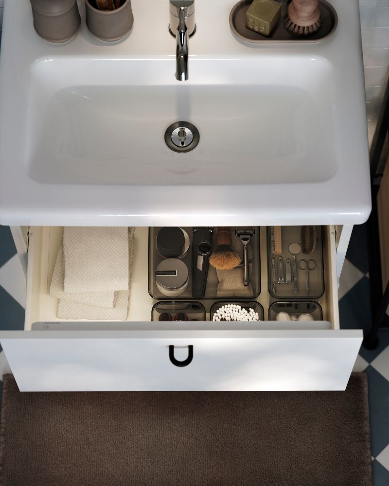 An aerial view of a white ENHET/TVÄLLEN vanity unit with basin. The top drawer is open, showing boxes with shaving products.