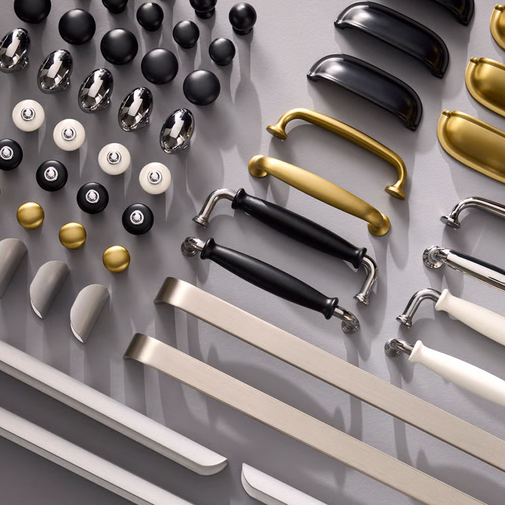 Handles and knobs for kitchen fronts, in dierent colours and dierent expressions, are placed in rows on a grey surface.