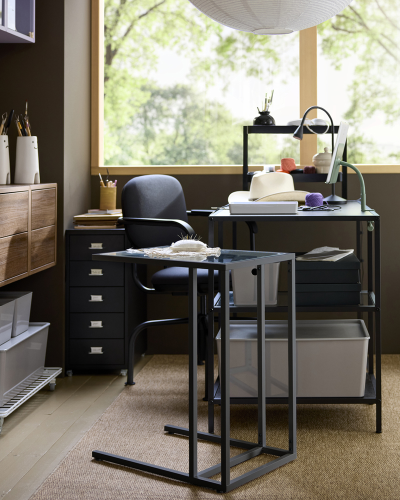 Home workspace setup with black-brown VITTSJÖ desk, a chair and storage drawers, placed by a bright window.
