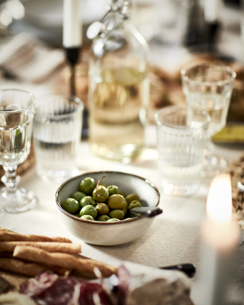 Bowl of green olives on a cozy dinner table with glasses, bottle, and candles.