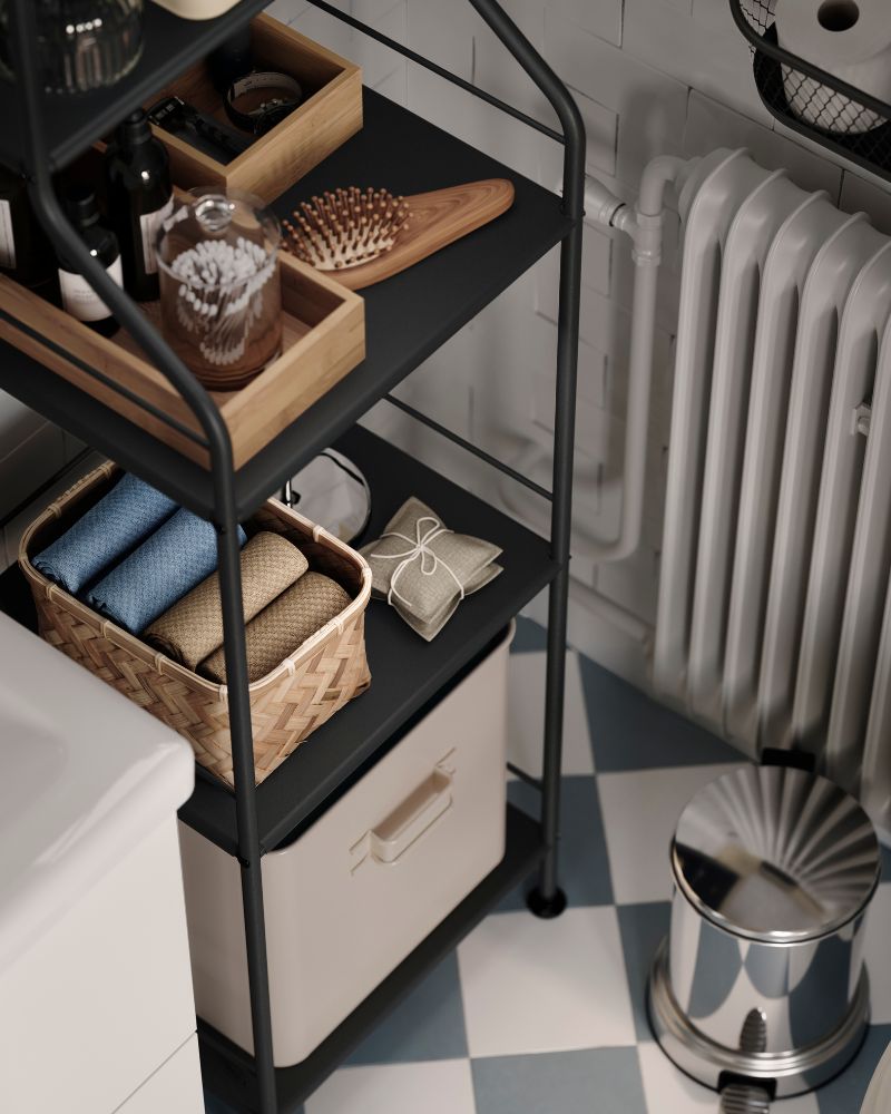 An aerial view of the lower part of a bathroom shelving unit, with a woven bamboo MJÖLKKANNA basket holding folded towels.
