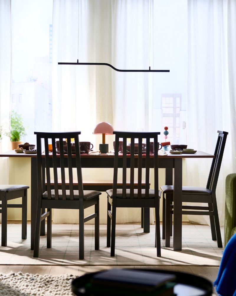 A dining area featuring an ÅLHULT extendable table surrounded by four chairs and accented by a PILSKOTT LED pendant lamp.