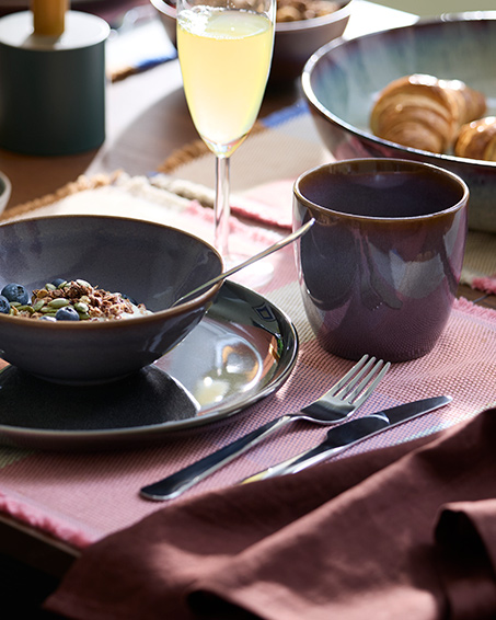 A bowl with yoghurt, muesli and blueberries are placed next to a lilac-coloured GLADELIG mug and a champagne flute.
