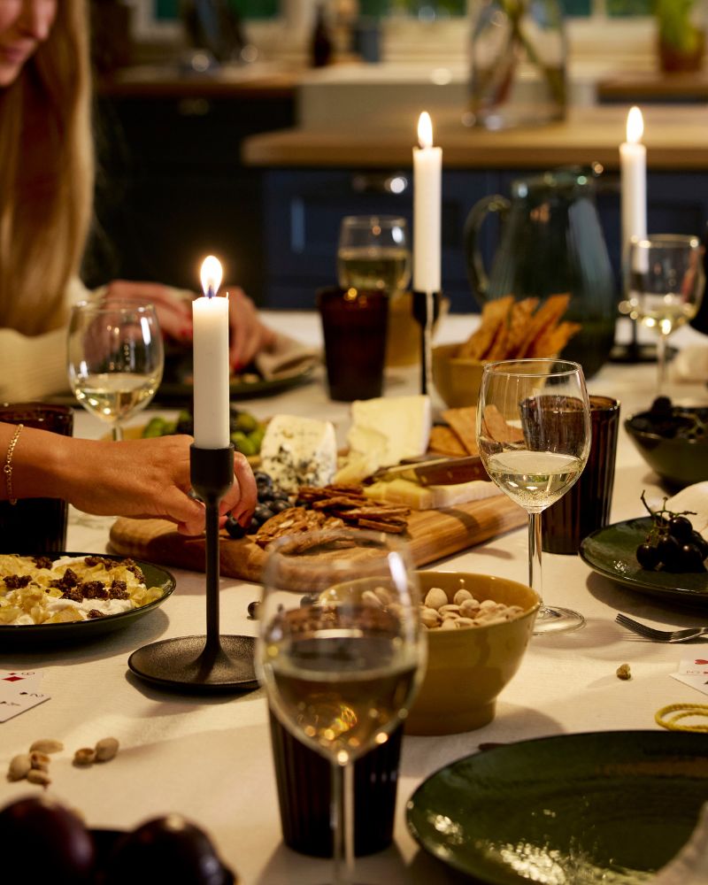 People are playing cards at a festive dinner table with candle sticks, wine glasses and plates with cheese and crackers.