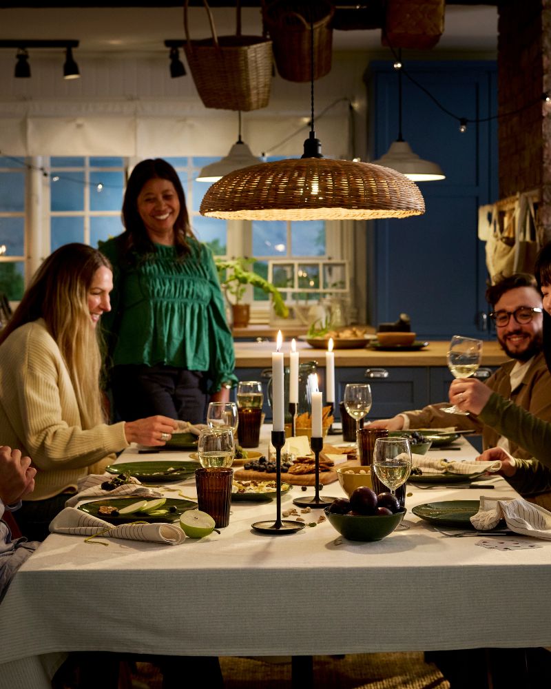 People are gathered around a dinner table for a meal of cheese and fresh fruit, all in a cosy, atmosphere with candles.
