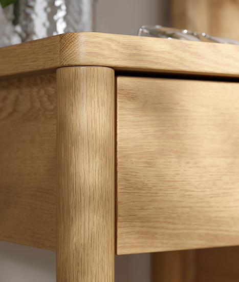 Detalle en primer plano de la esquina redondeada de una mesa auxiliar de madera clara con acabado suave.