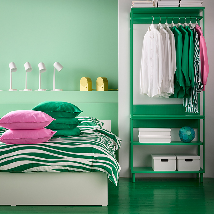 Modern IKEA bedroom with green striped bedding, pink pillows, and open green wardrobe. Stylish storage solutions for an organized and inspiring space.