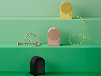Portable IKEA speakers in various colors on green shelves. Sound and design for any corner of your home.