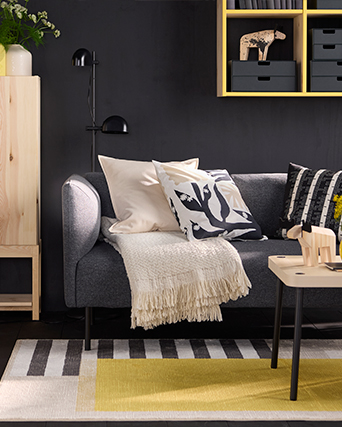 Cozy IKEA living room with gray sofa, cushions, and blanket. Storage solutions with yellow shelving for a functional and stylish space.
