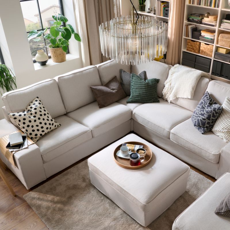 A light, bright living room with a KIVIK corner  sofa and with colourful cushions, a throw and a  centrally placed footstool.