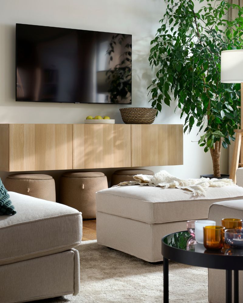 A light, bright living room with a combination  of KIVIK seating, a STOENSE rug, a wall-hung  TV and a big, leafy plant.