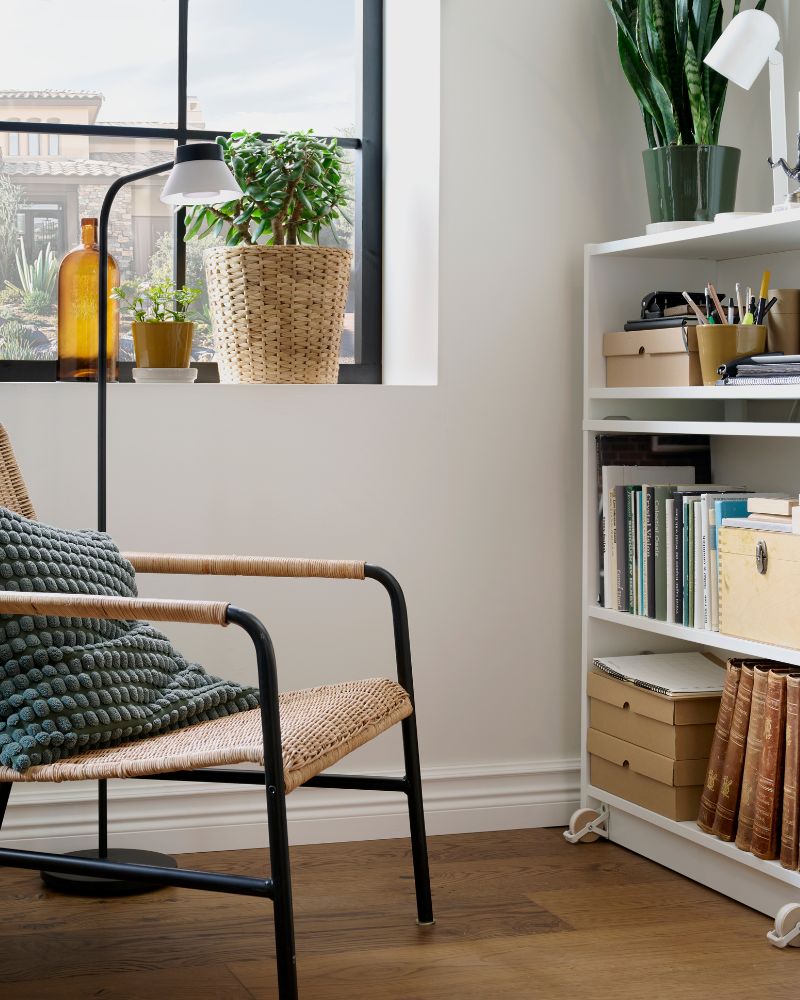A bright corner with an ULRIKSBERG rattan  armchair by a window and next to BILLY  bookcases filled with desk accessories.