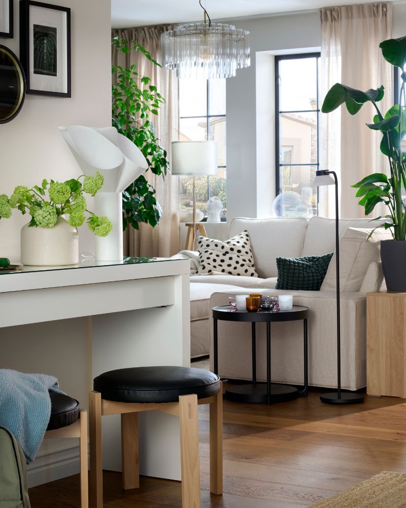A bright hallway and living room centred  around a KIVIK sofa surrounded by plants and  textiles, and flanked by large windows.