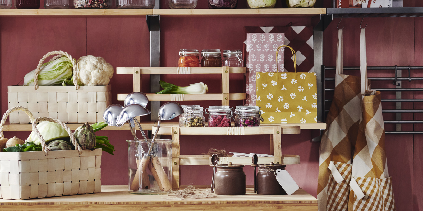A kitchen with shelves and a table adorned with several KÖSSEBÄR items, like jars, baskets, tea towels, aprons, and more.