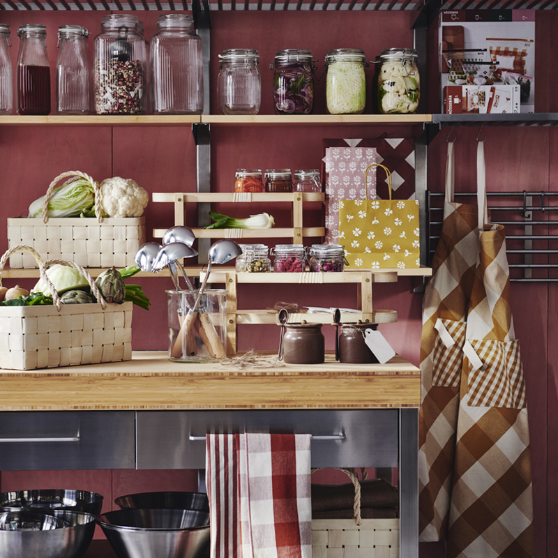 A kitchen with shelves and a table adorned with several KÖSSEBÄR items, like jars, baskets, tea towels, aprons, and more.