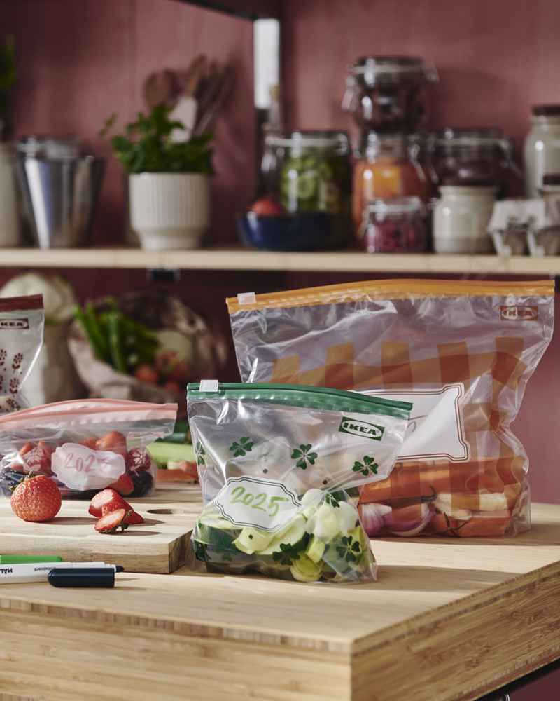 Four various-coloured KÖSSEBÄR resealable bags filled with vegetables, berries, and mushroom sit on a worktop.