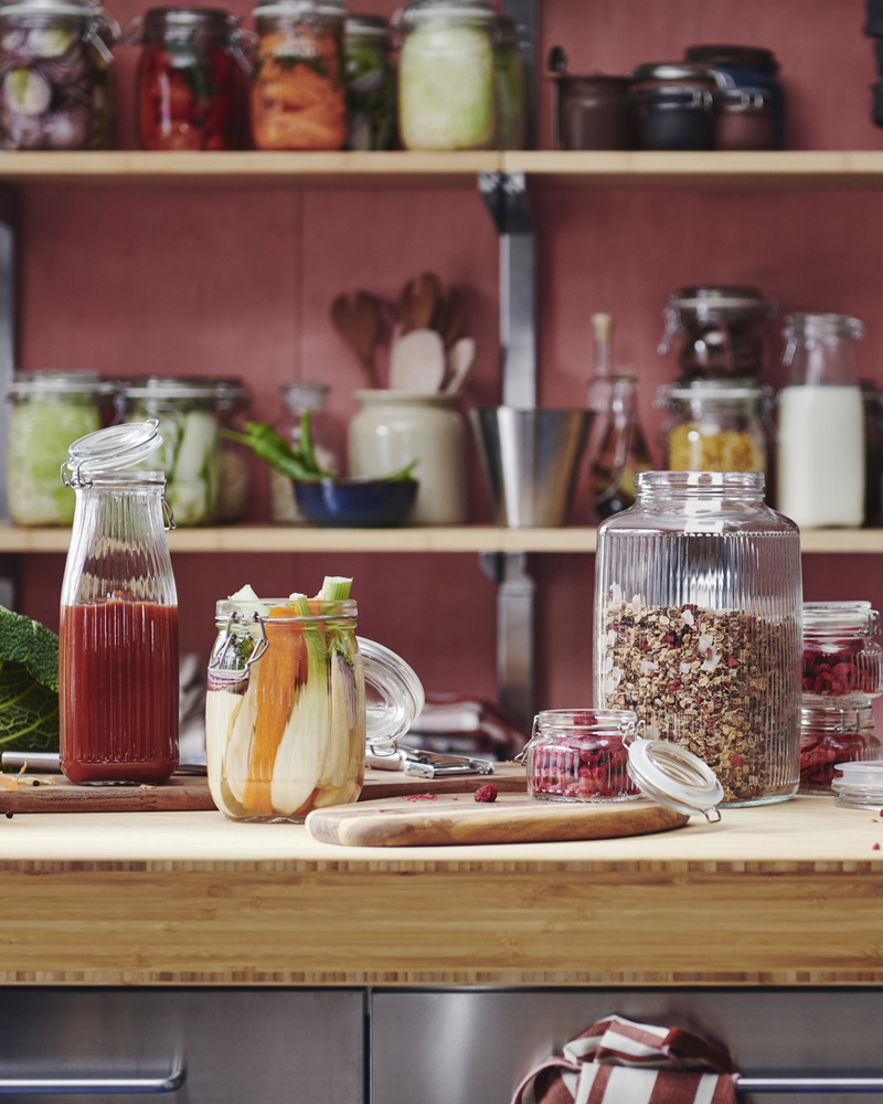 A KÖSSEBÄR jar with lid sits beside other jars in different shapes, all filled with food and drinks, on a bamboo worktop.