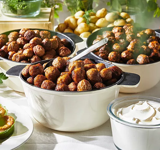 Three large bowls of steamed cooked meat or vegetarian meatballs, accompanied by boiled potatoes and a bowl of white sauce, arranged on a table for serving.
