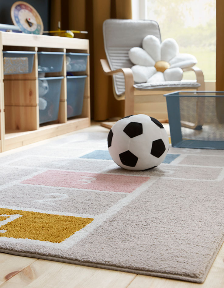 A STÄPPSPARV rug featuring a hopscotch pattern placed in a children’s room with a textile football and mesh storage units