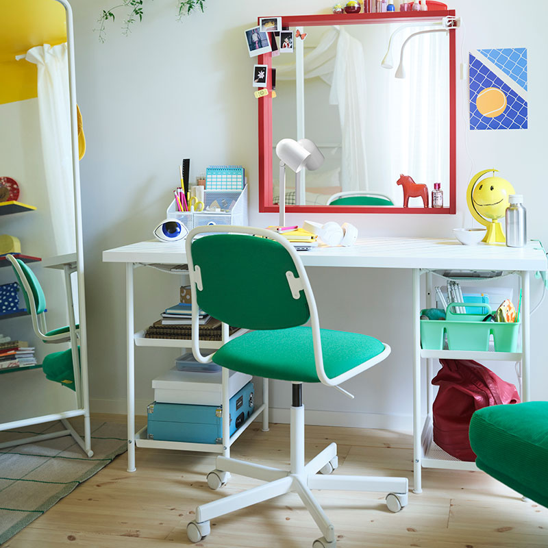 A teen bedroom with a large white bed, a desk with a big red mirror above it, a green desk chair and armchair, and more.