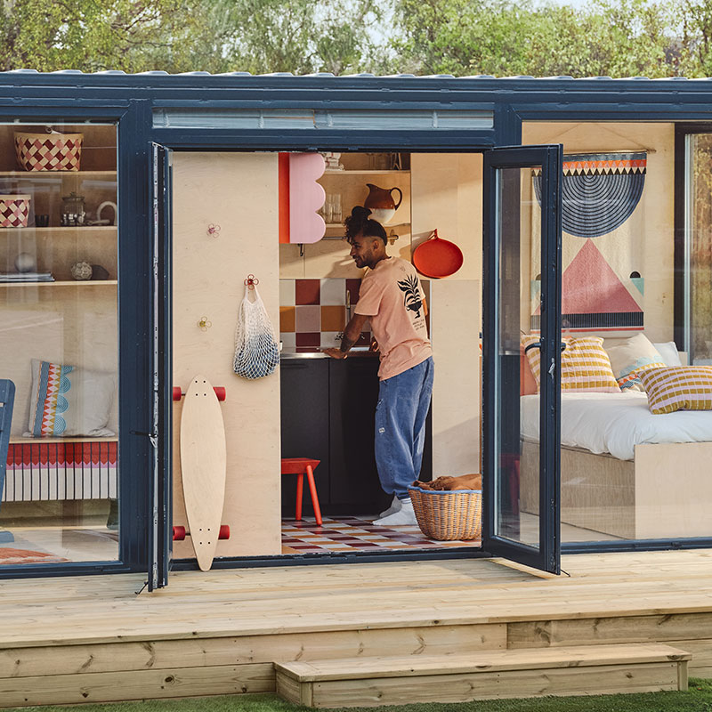 Apartment made from shipping containers, with windows to the bedroom and living room; open door shows IKEA OMMJÄNGE items.