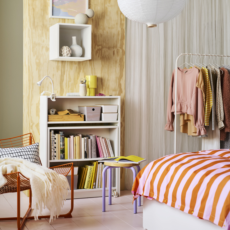 A white BILLY bookshelf with foldable table against a light wood wall with a NÄVLINGE LED clamp spotlight on the top shelf.
