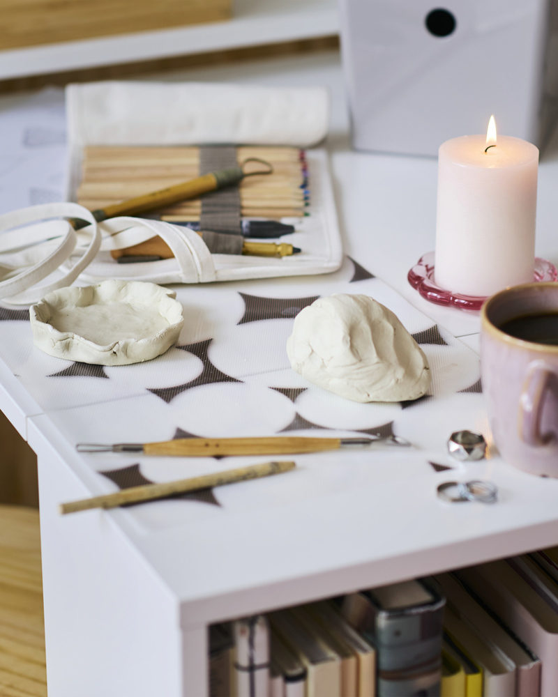 SOLFÅGEL pencil set in a roll-up pencil case and a pink cup on the fold-out table of a BILLY bookcase with foldable table.