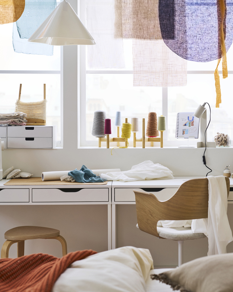 Two white ALEX desks in a sunny bedroom placed side by side create a hobby area with a FJÄLLBERGET conference chair in front.