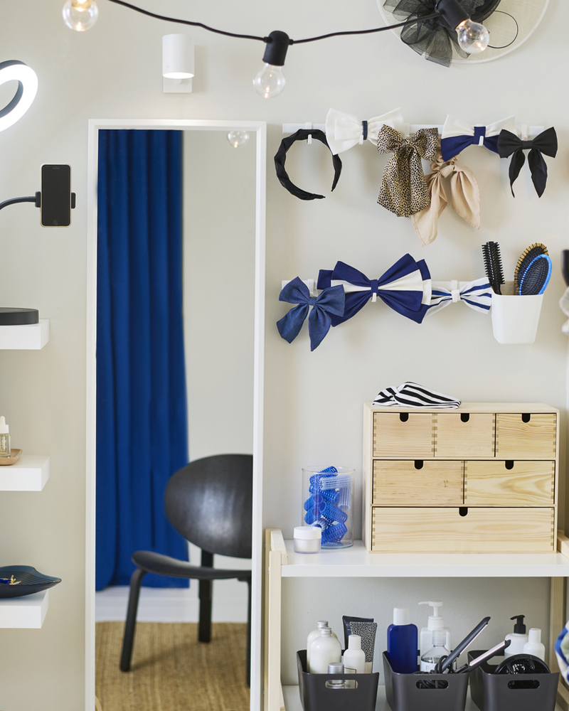 A pine MOPPE mini chest on a white shelf with hair acessories around it. A white NISSEDAL mirror is on the wall beside it.