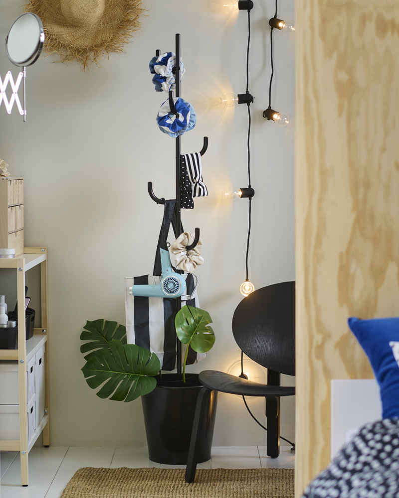 A black ÄLGANÄS hat and coat stand holds hair accessories with a SVARTRÅ LED light chain and a FRÖSET easy chair beside it.