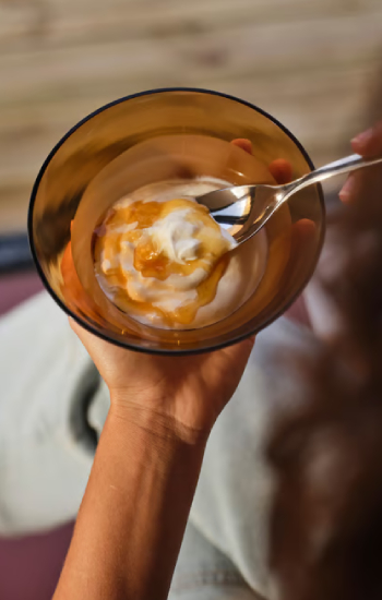 Hand holding a small dark glass bowl with yogurt and honey.