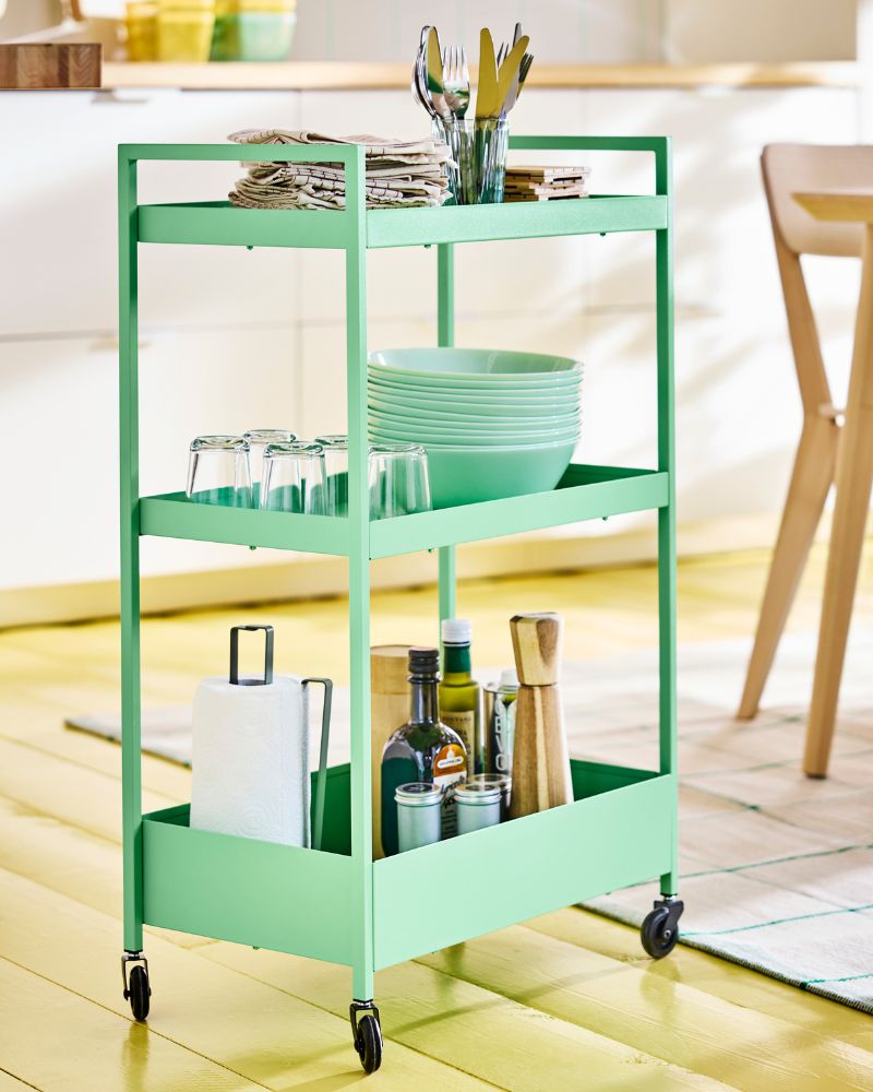 Light green NISSAFORS drinks trolley on  wheels loaded with bowls, plates and other  dinnerware in a modern kitchen setting.